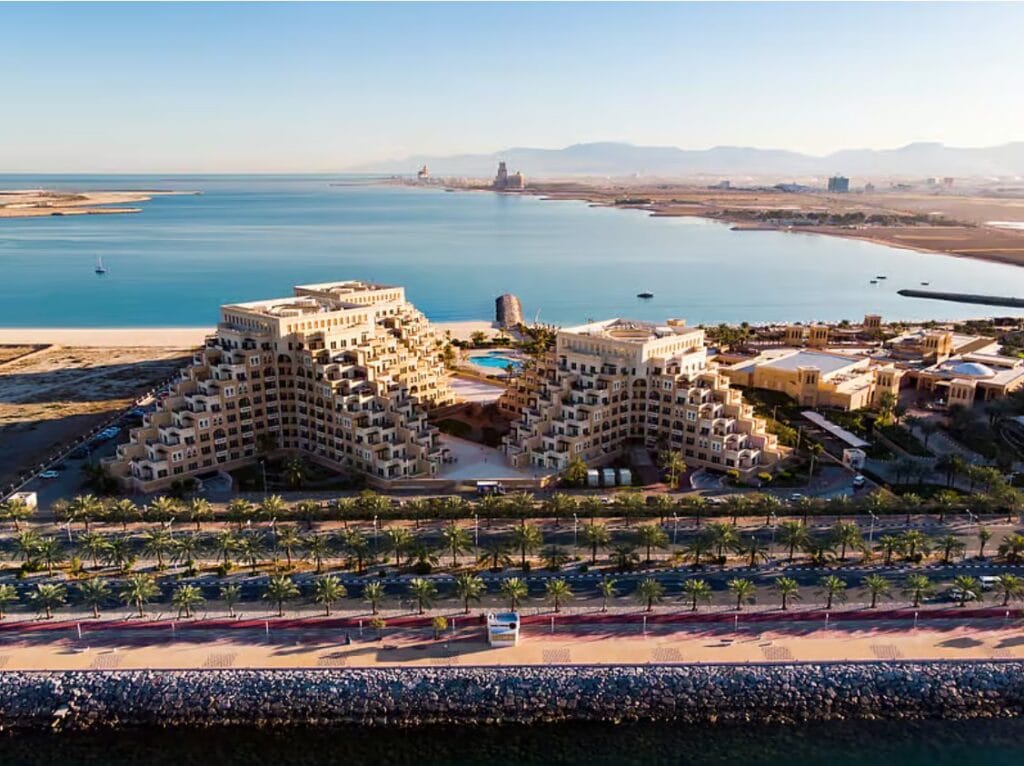 Aerial view of beachfront residences and palm-lined promenade in Ras Al Khaimah with the Hajar Mountains in the distance